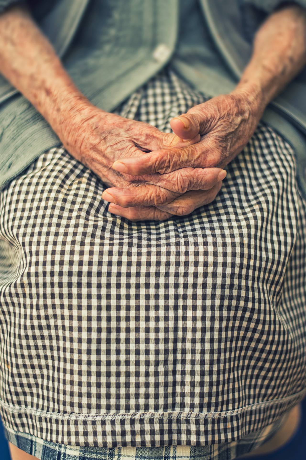 The folded hands of an older person resting in their lap
